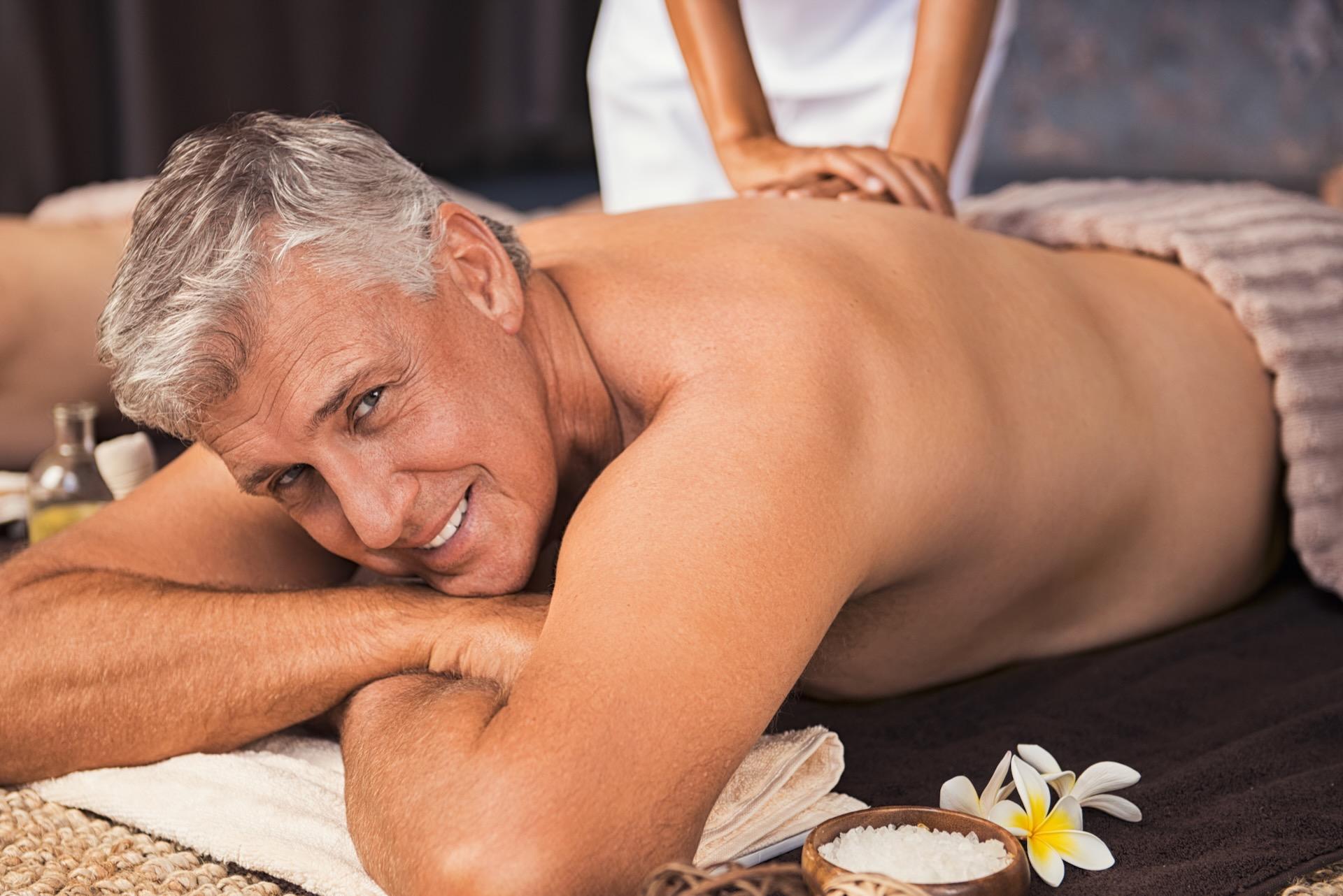 Senior man relaxed in spa while having a back massage. Happy mature man feeling relaxed and looking at camera. Male beauty therapy concept.