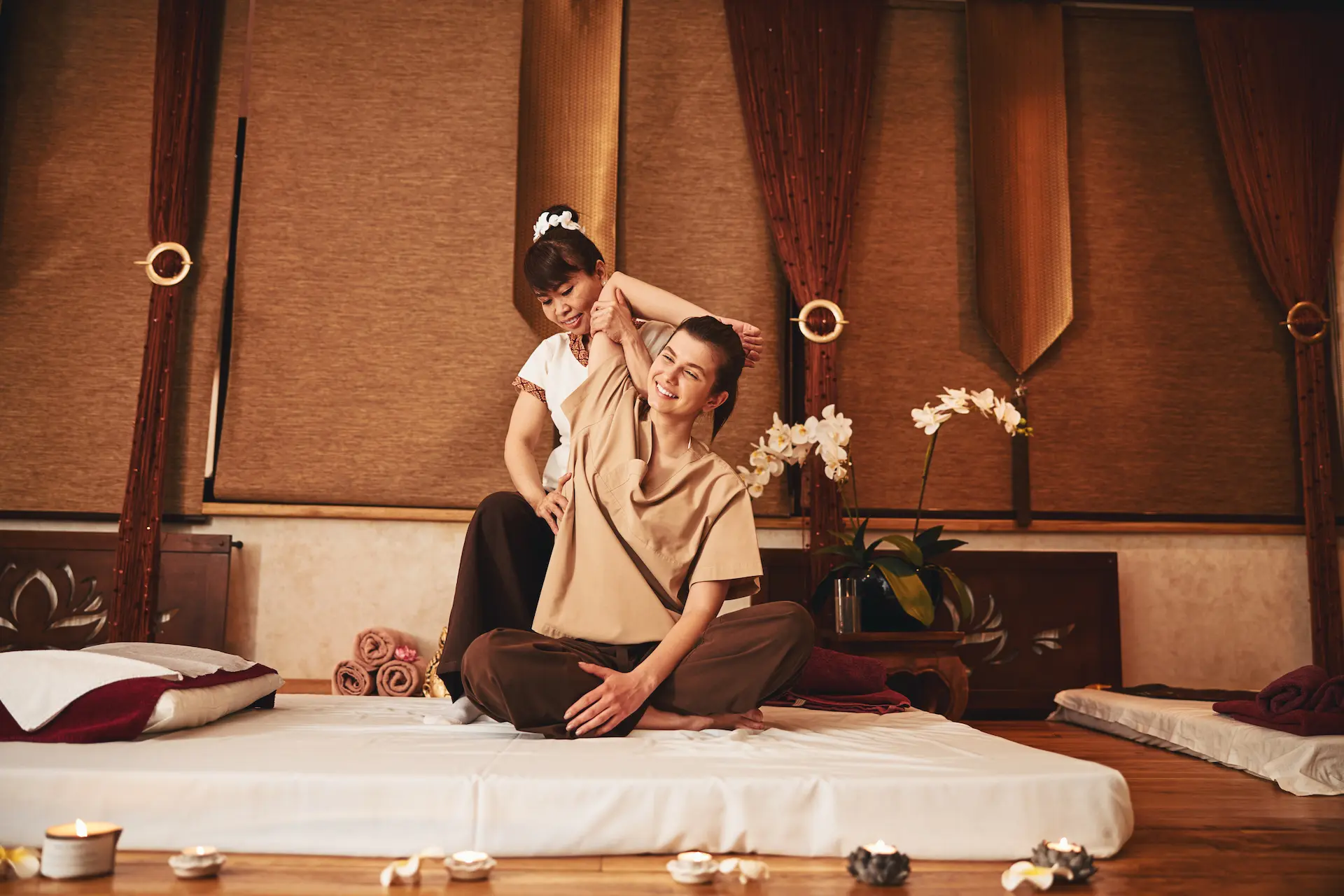 The Thai massage specialist is lifting the right arm of the smiling woman while pressing her palm to the client's waist.
